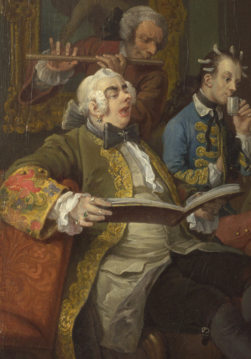 A large man in a fur-trimmed coat and earrings singing from a music book with his mouth open, a flute player behind him, a man in blue drinking chocolate beside them